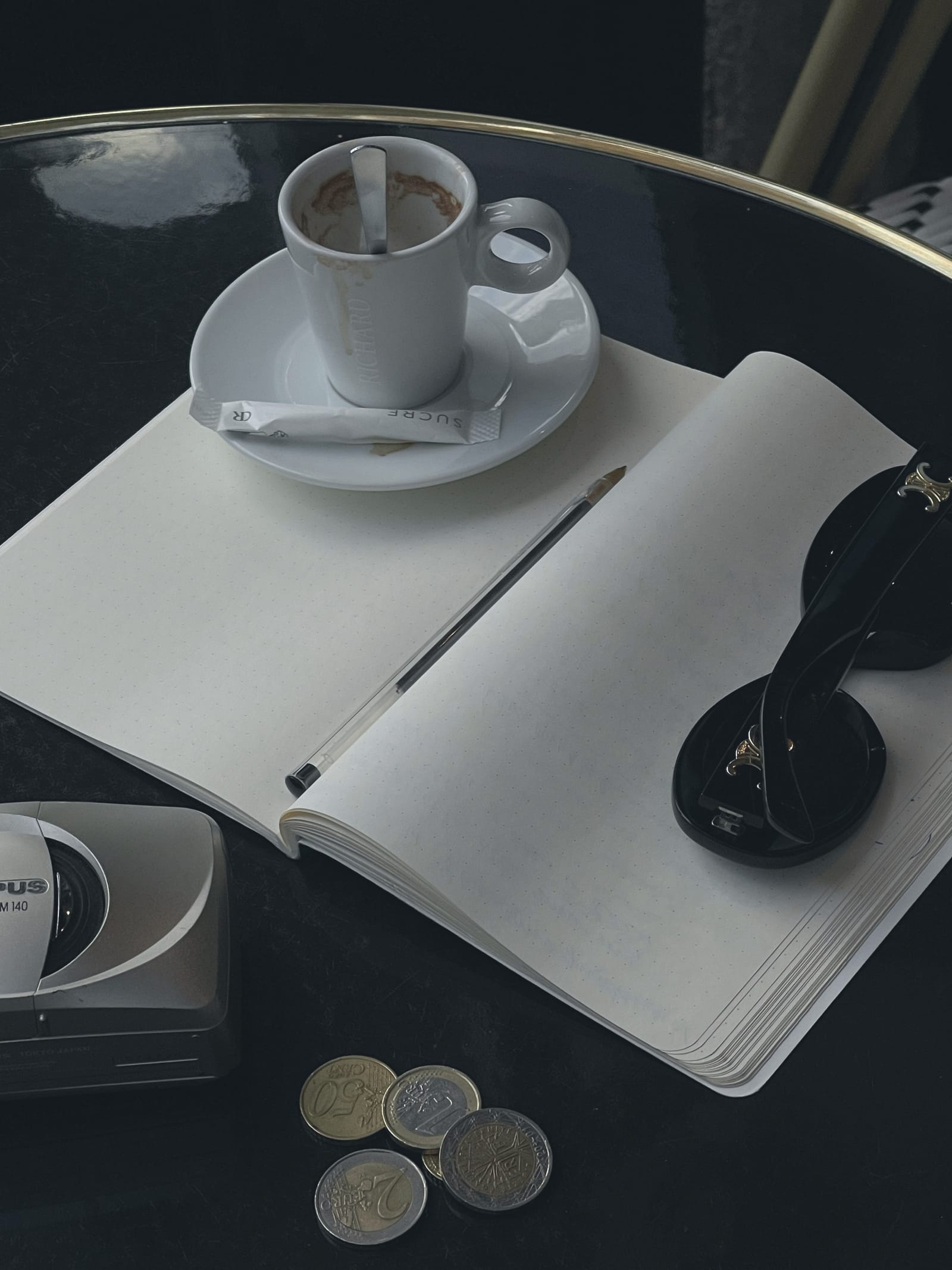 Koyu bir kafe masasında açık bir defter, üzerinde kalem ve yanında bir fincan.
