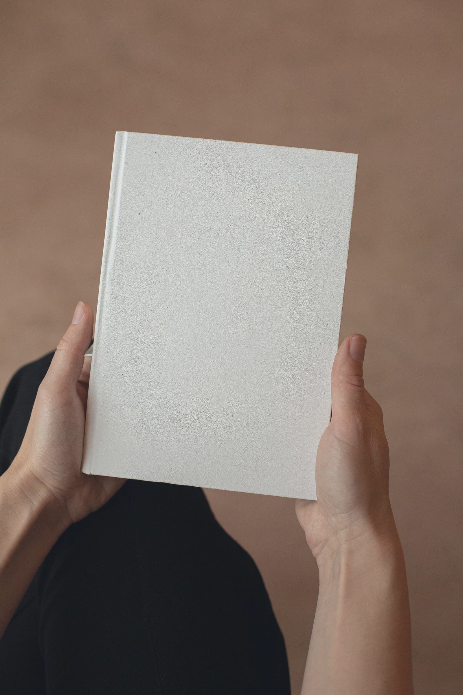 İki elin arasında tutulan, kapağı boş, kapalı bir defter.